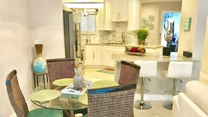A modern kitchen with white cabinets, a marble countertop, and a dining area with a glass table and wicker chairs.