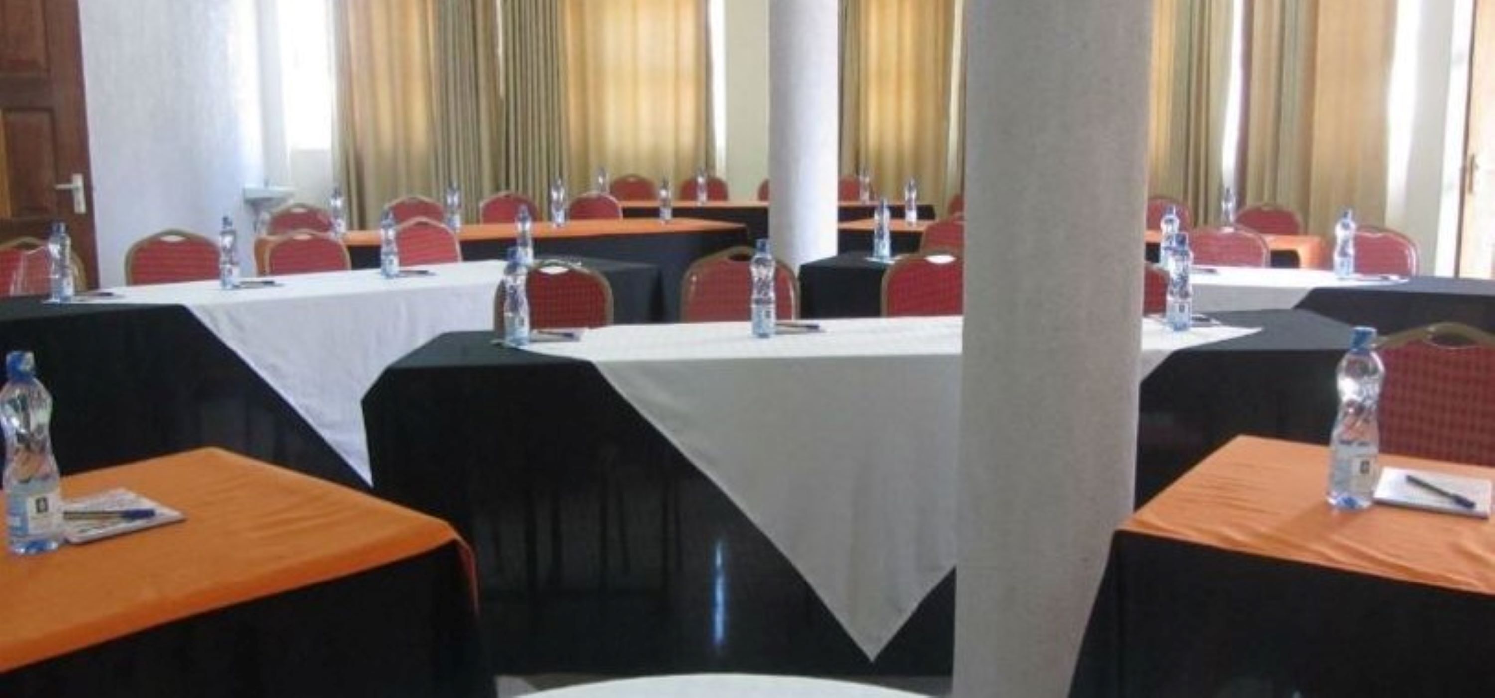 A conference room with multiple tables, each with a white tablecloth, red chairs, and water bottles.