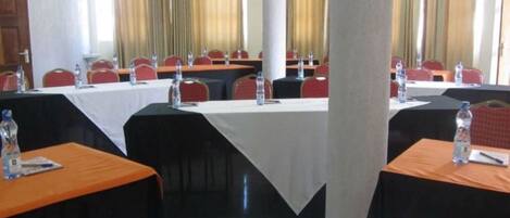 A conference room with multiple tables, each with a white tablecloth, red chairs, and water bottles.