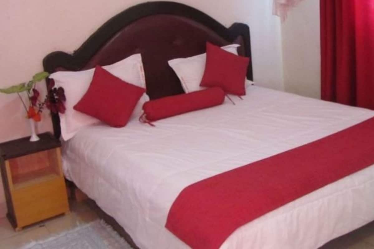 Uma cama com colcha branca e vermelha, cabeceira de madeira e cortinas vermelhas.