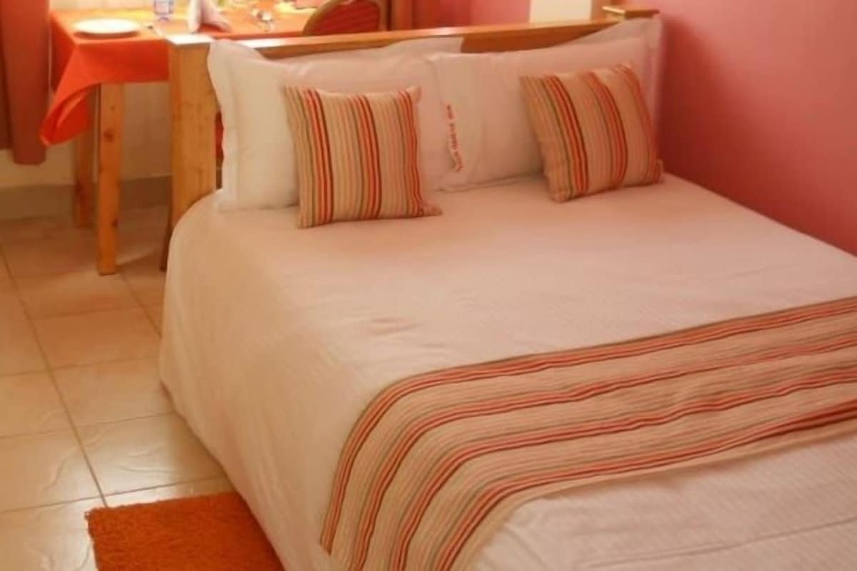 Un dormitorio con una cama, almohadas, una mesa con una silla y una alfombra pequeña.