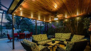 Eine Terrasse im Freien mit Holzboden und Lichterketten, umgeben von Korbmöbeln und roten Stühlen.