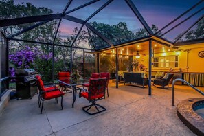Une terrasse extérieure couverte, avec des chaises rouges, un barbecue et un jacuzzi.