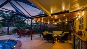 Eine überdachte Terrasse im Freien mit Whirlpool, Sitzgelegenheit und Blick auf den umliegenden Garten.