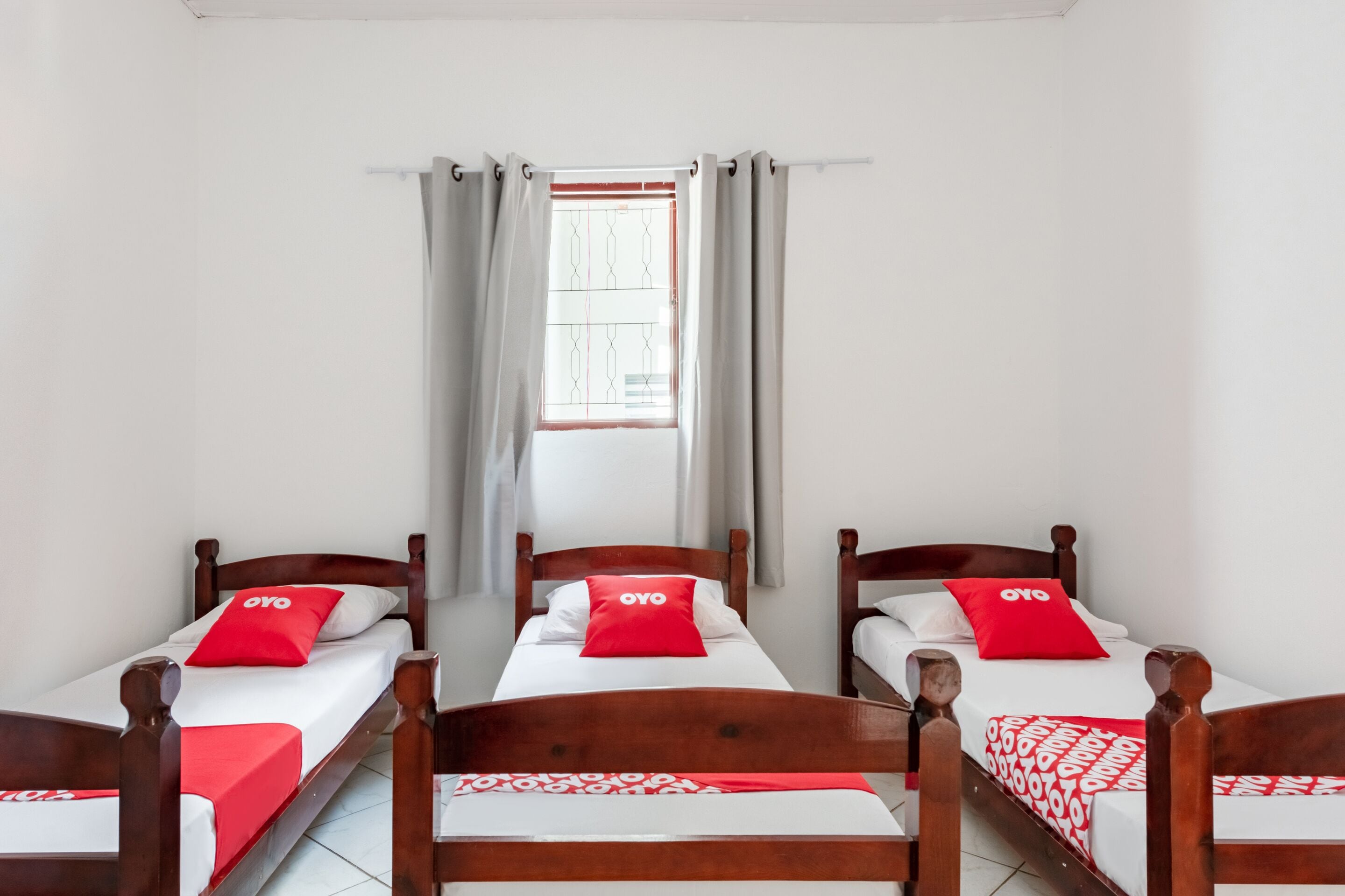 Una habitación con tres camas de madera, cada una con una almohada roja y una colcha blanca.