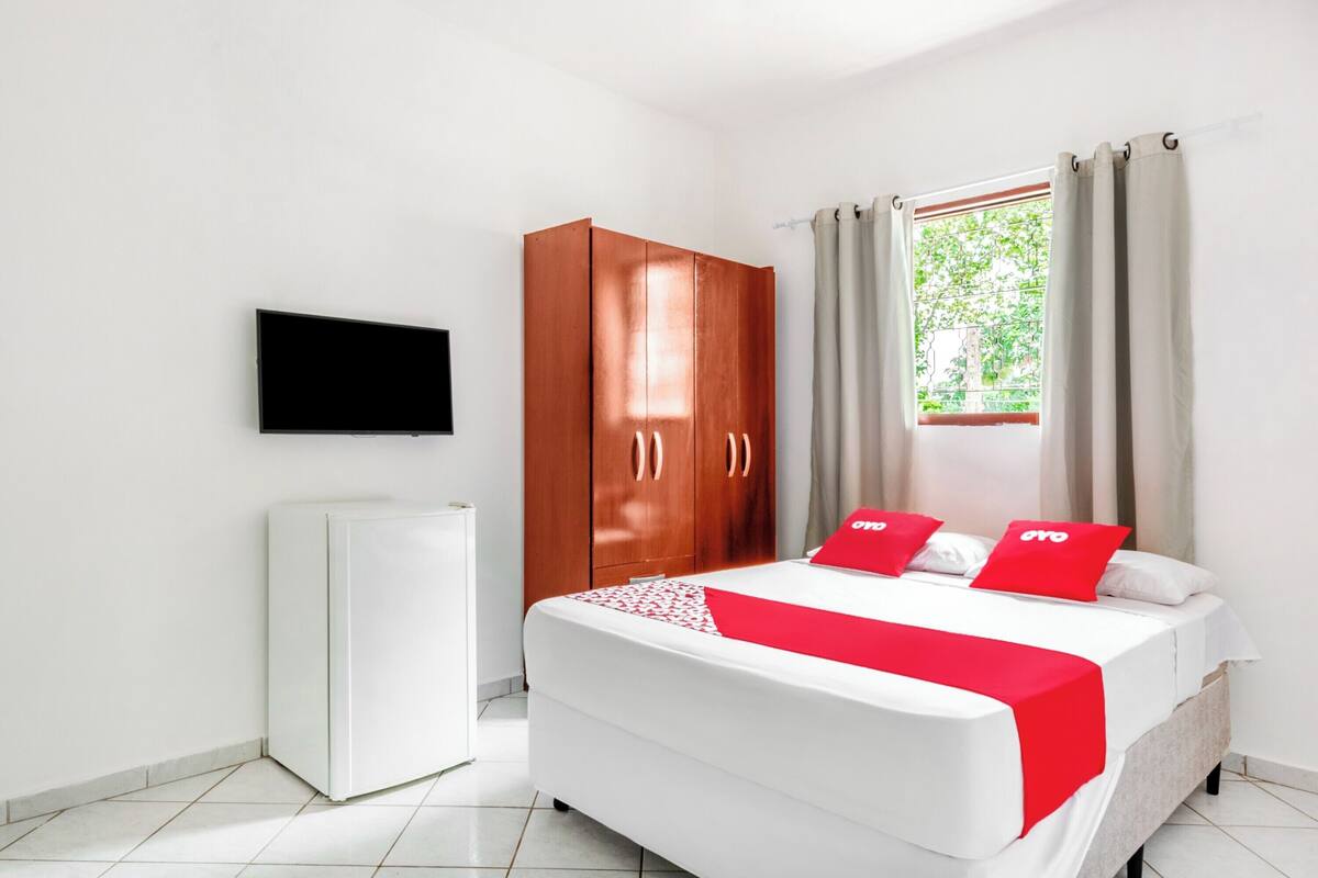 A hotel room with a bed, a wardrobe, a television, and a window with curtains.