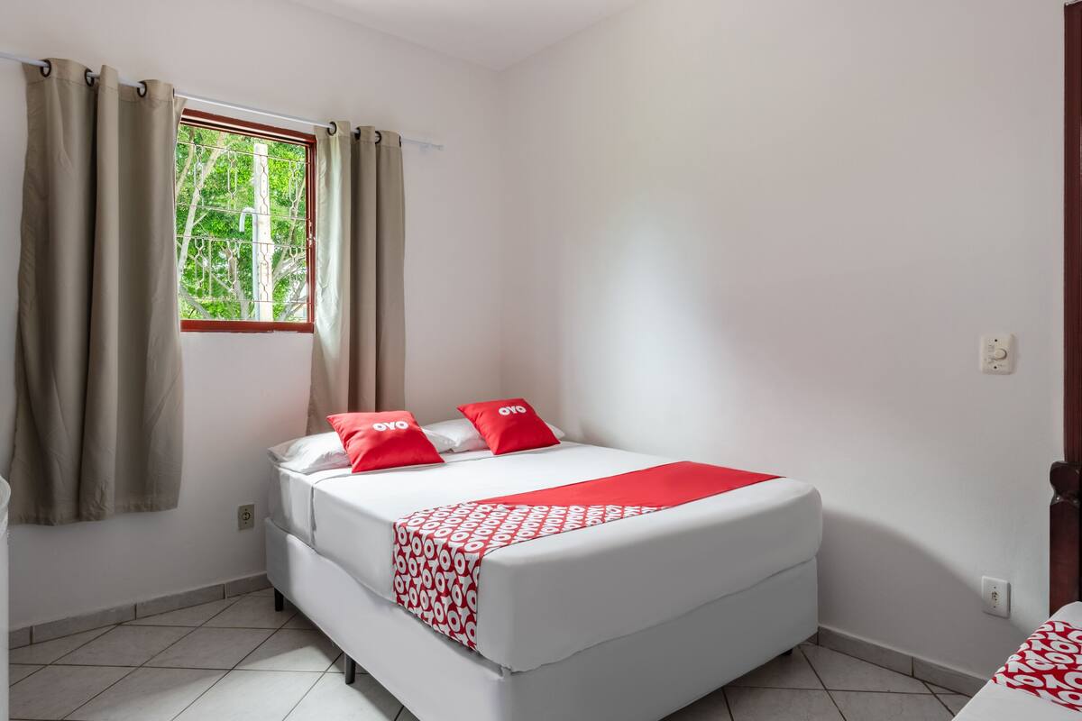 A single-bed room with a window, white walls, and a tiled floor.