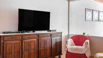 Een houten kast met een flatscreen televisie, een rode stoel met een witte bekleding, en ingelijste kunstwerken aan de muur.