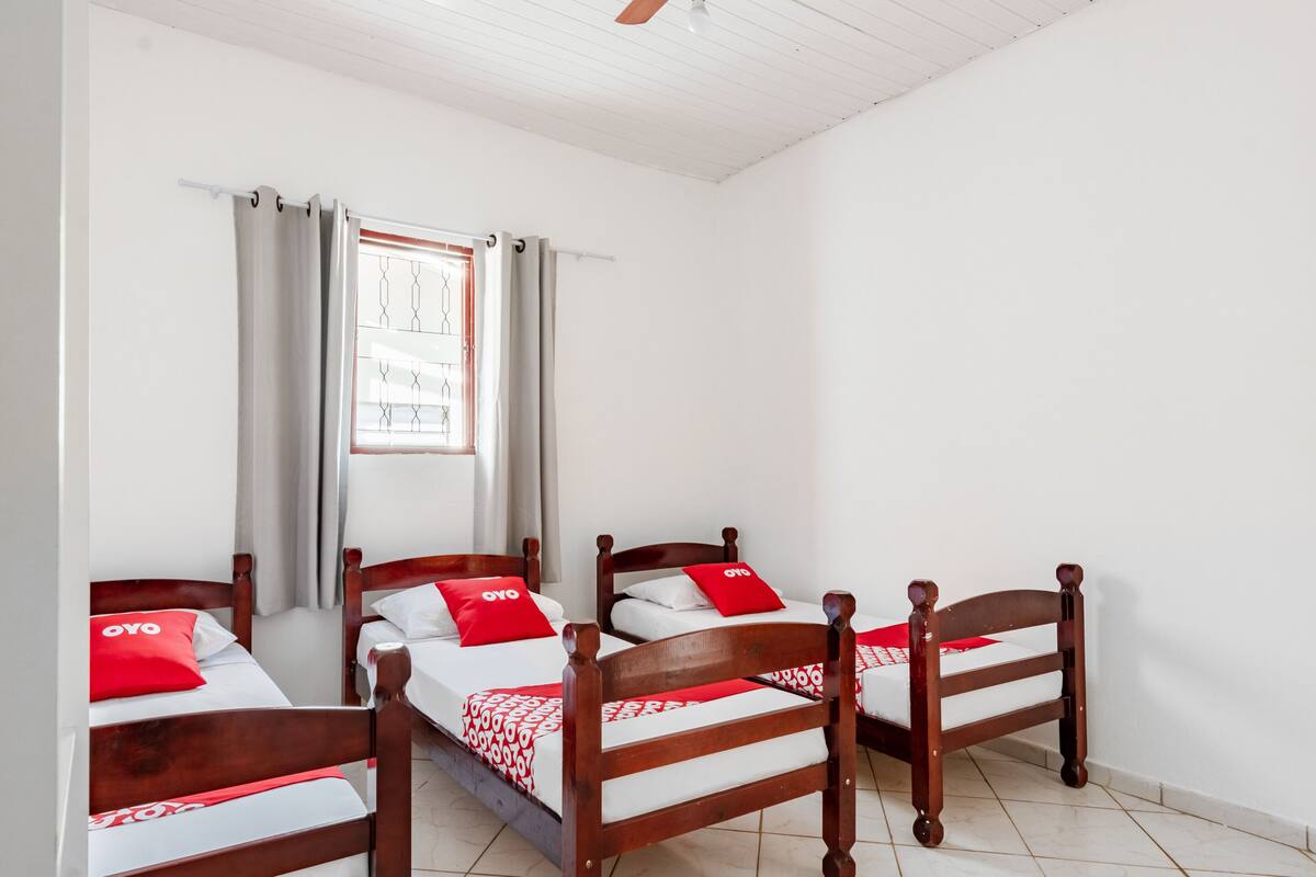 A room with four wooden beds, each with a red and white patterned bedspread and a red pillow with "OYO" branding.