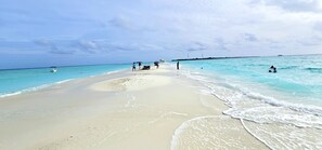 A beach with clear turquoise water, a boat in the distance, and people enjoying the shore. - Beach Cottage (Rasdhoo)