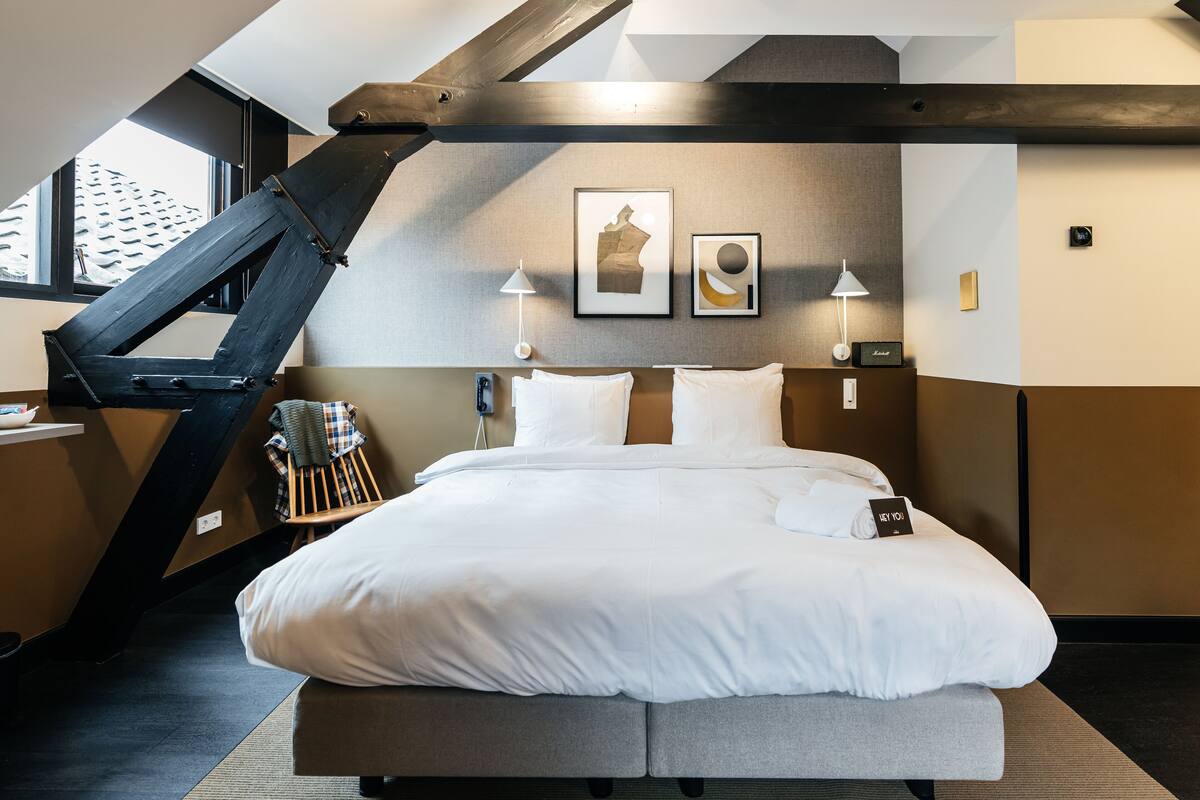 A modern hotel room with a large bed, a desk, and a chair. There is a window with a view of a building outside.