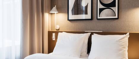 A hotel room with a neatly made bed, a lamp, and two framed artworks on the wall.