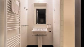 Een smalle badkamer met een wastafel op een voetstuk, een spiegel erboven en een handdoekrek aan de linkerkant.