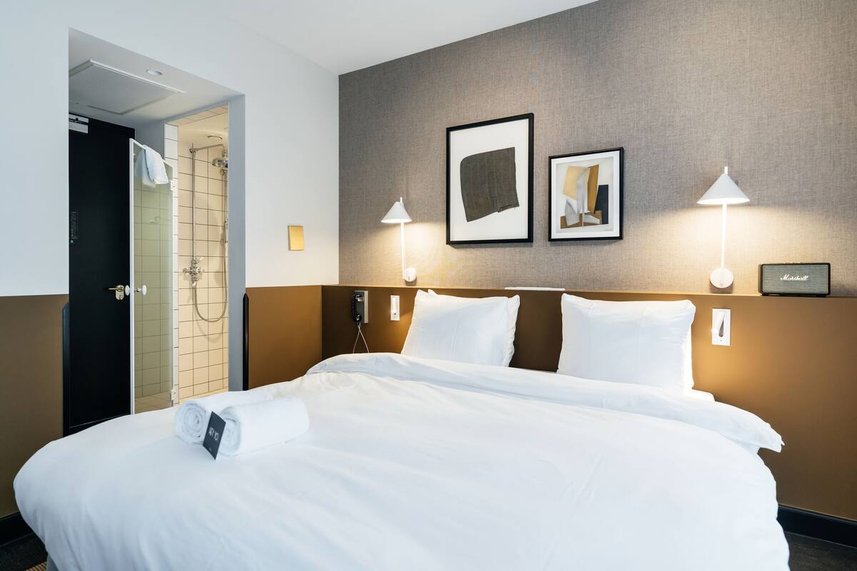 A hotel room with a large bed, a shower area, and two wall-mounted lamps.