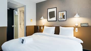 Habitación de hotel con una cama grande, zona de ducha y dos lámparas fijadas a la pared.