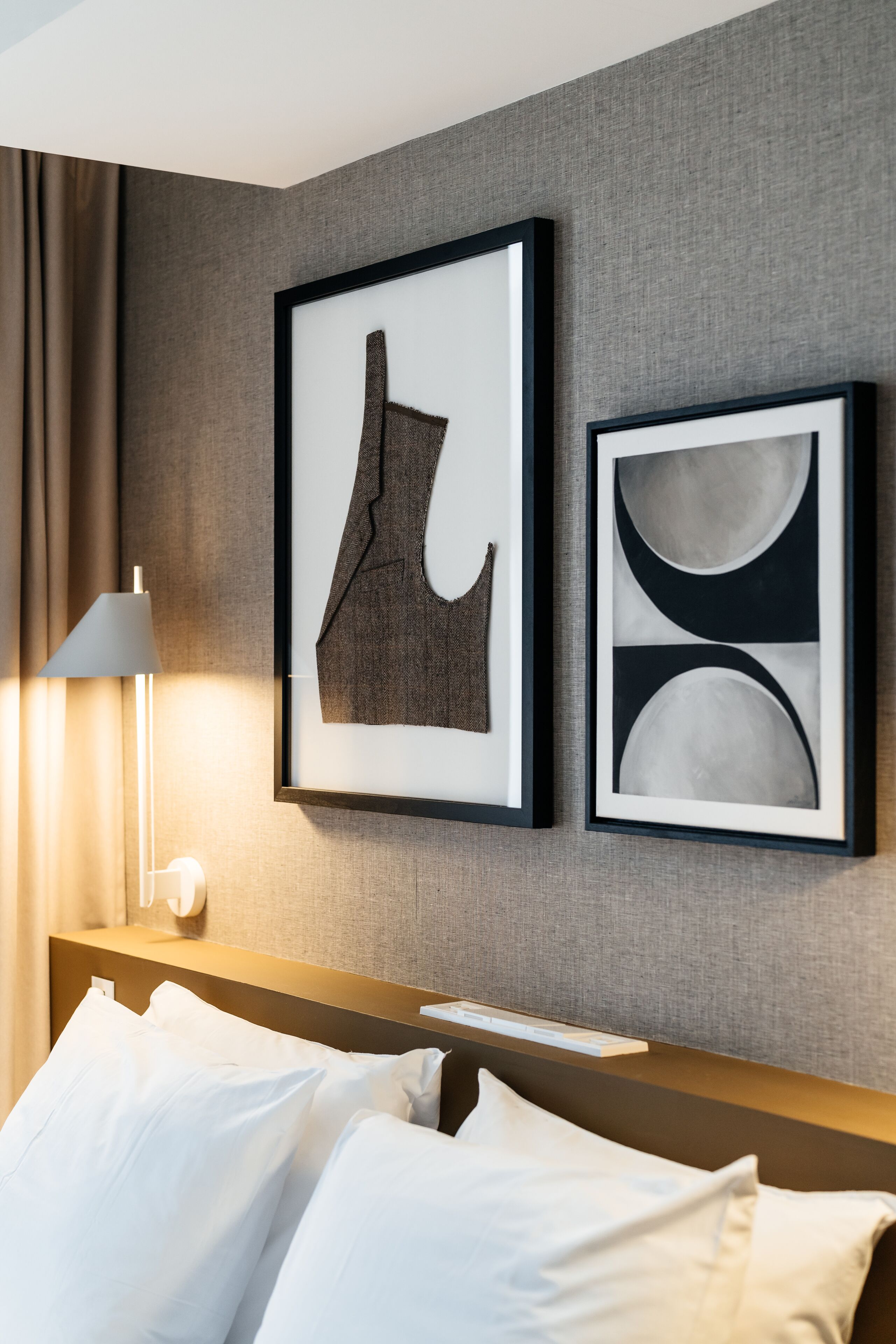 A hotel room with a bed, a nightstand, a lamp, and two framed artworks on the wall.