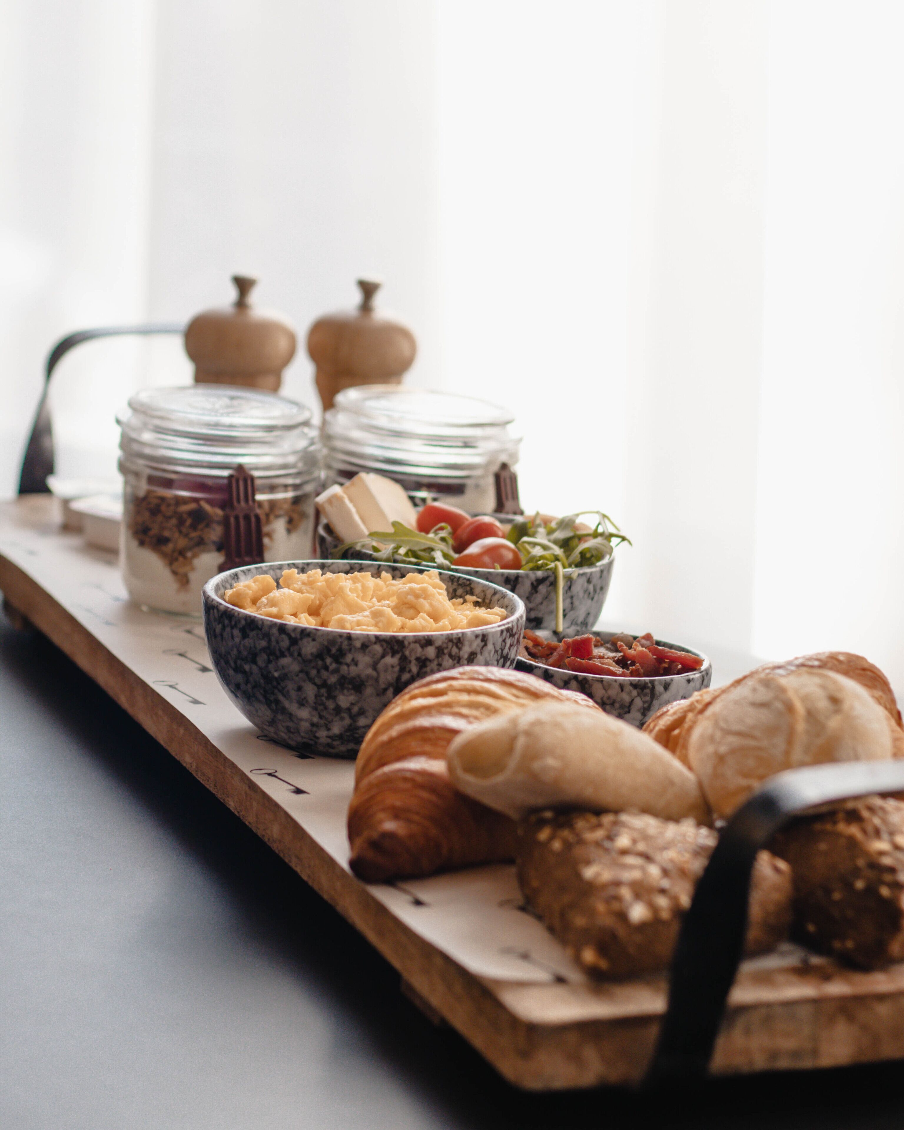 A breakfast spread with pastries, cheese, and jams on a wooden board.