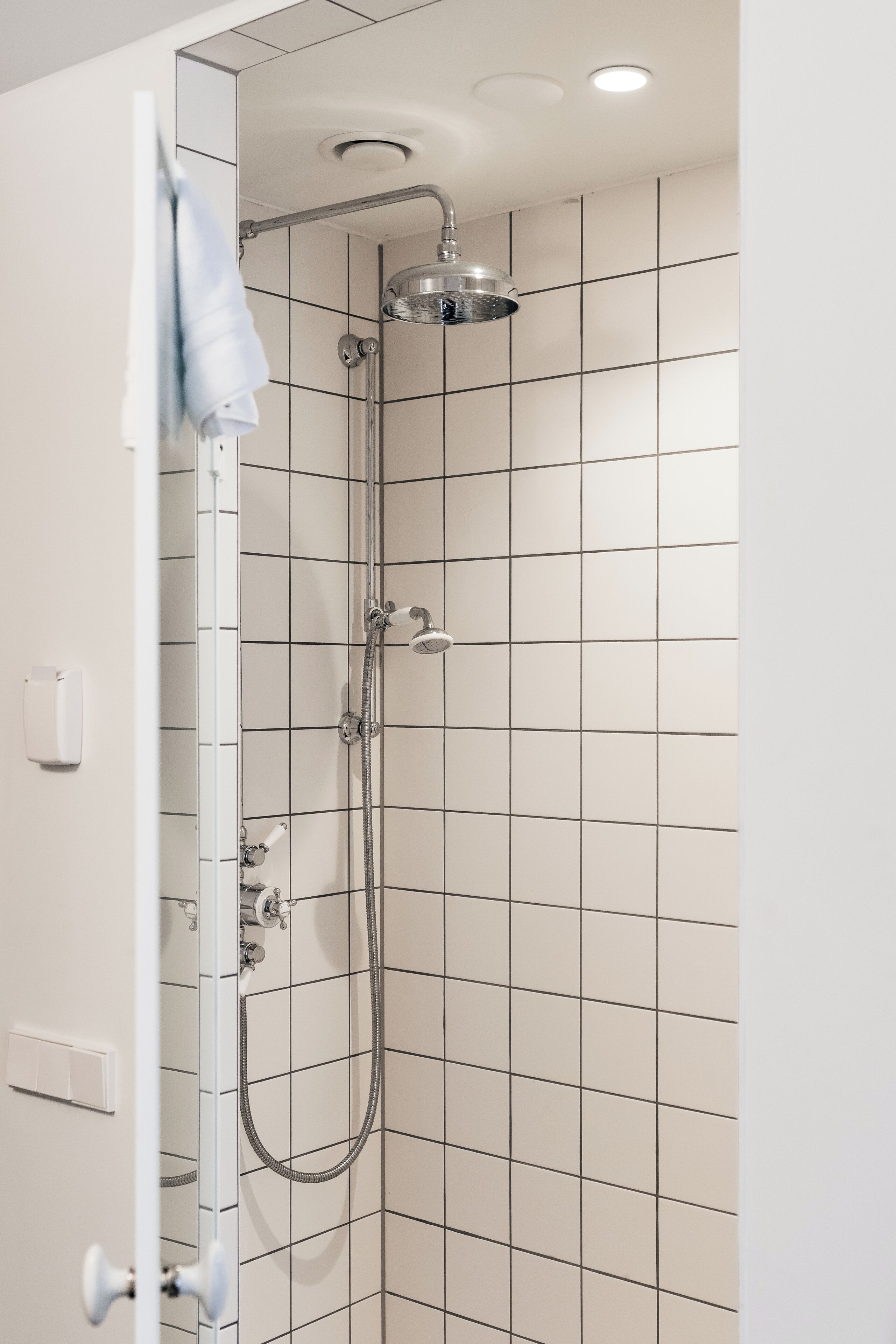 A shower with a handheld showerhead and a wall-mounted faucet, tiled walls, and a towel hanging on a rack.