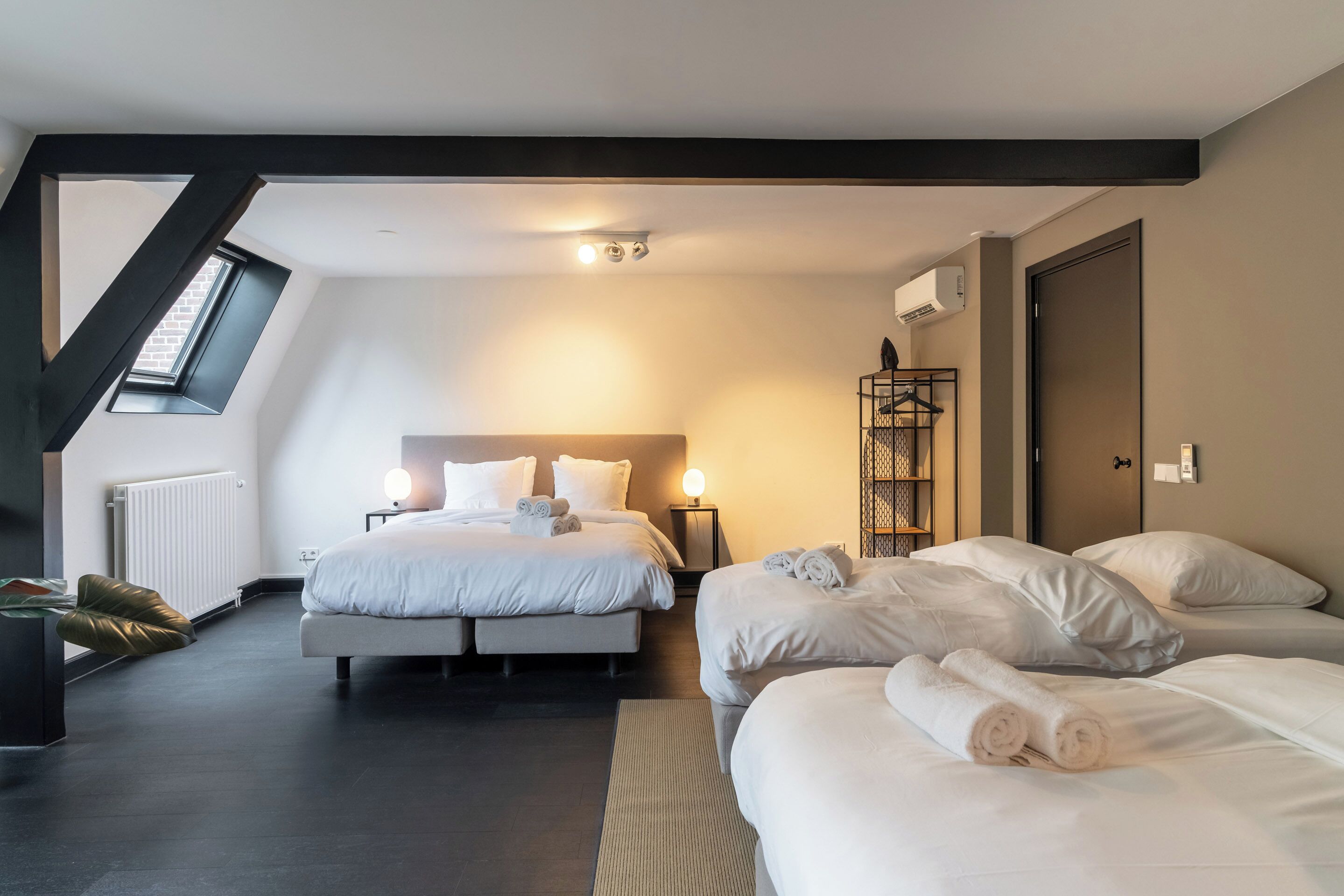 A modern hotel room with two beds, a skylight, a radiator, and a wardrobe.