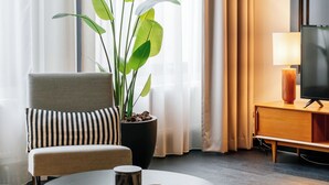 A modern hotel room with a comfortable chair, a round coffee table, a potted plant, a television, and a lamp. - The Hunfeld (Utrecht)
