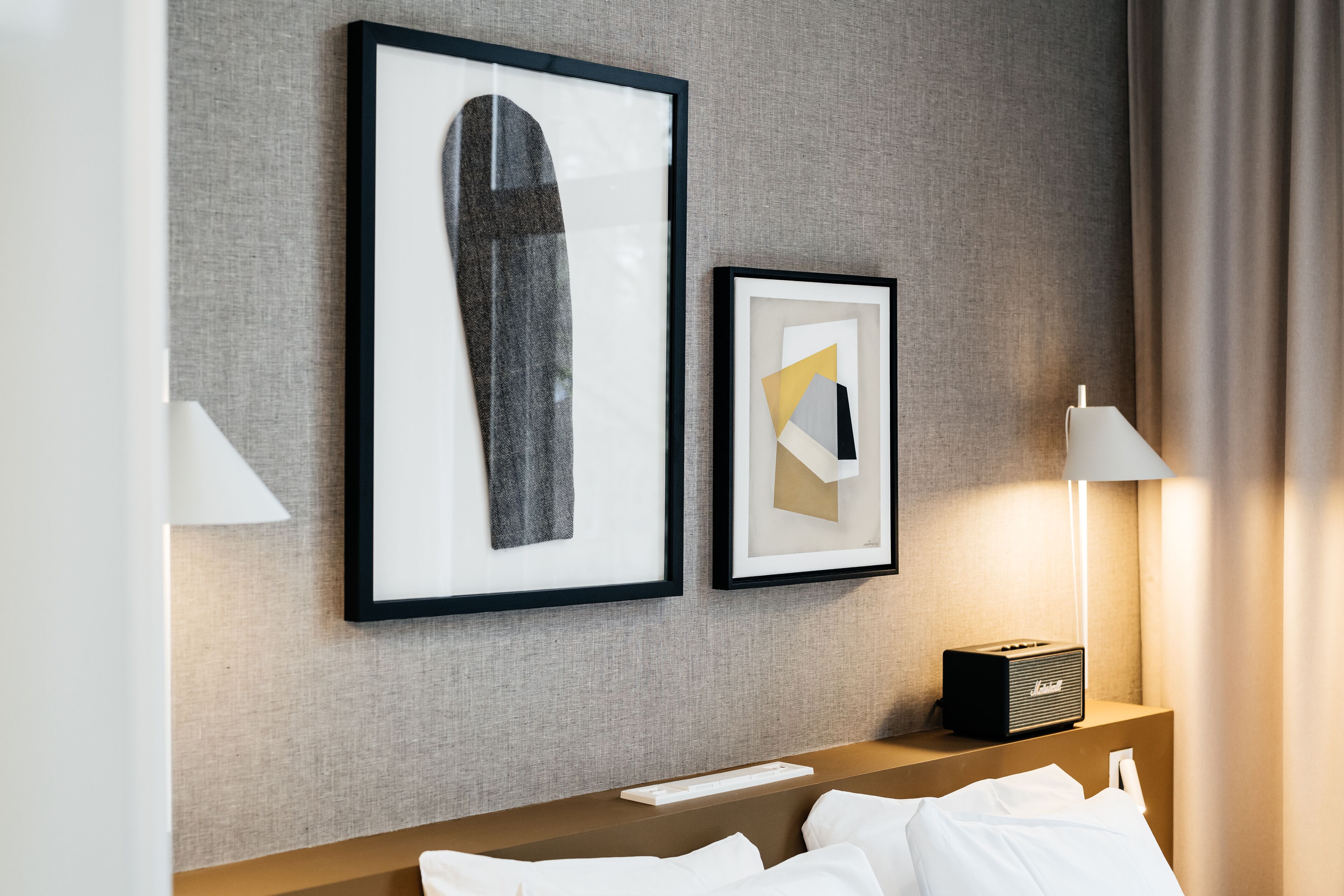 Een hotelkamer met een bed, een nachtkastje met een lamp en twee ingelijste kunstwerken aan de muur.