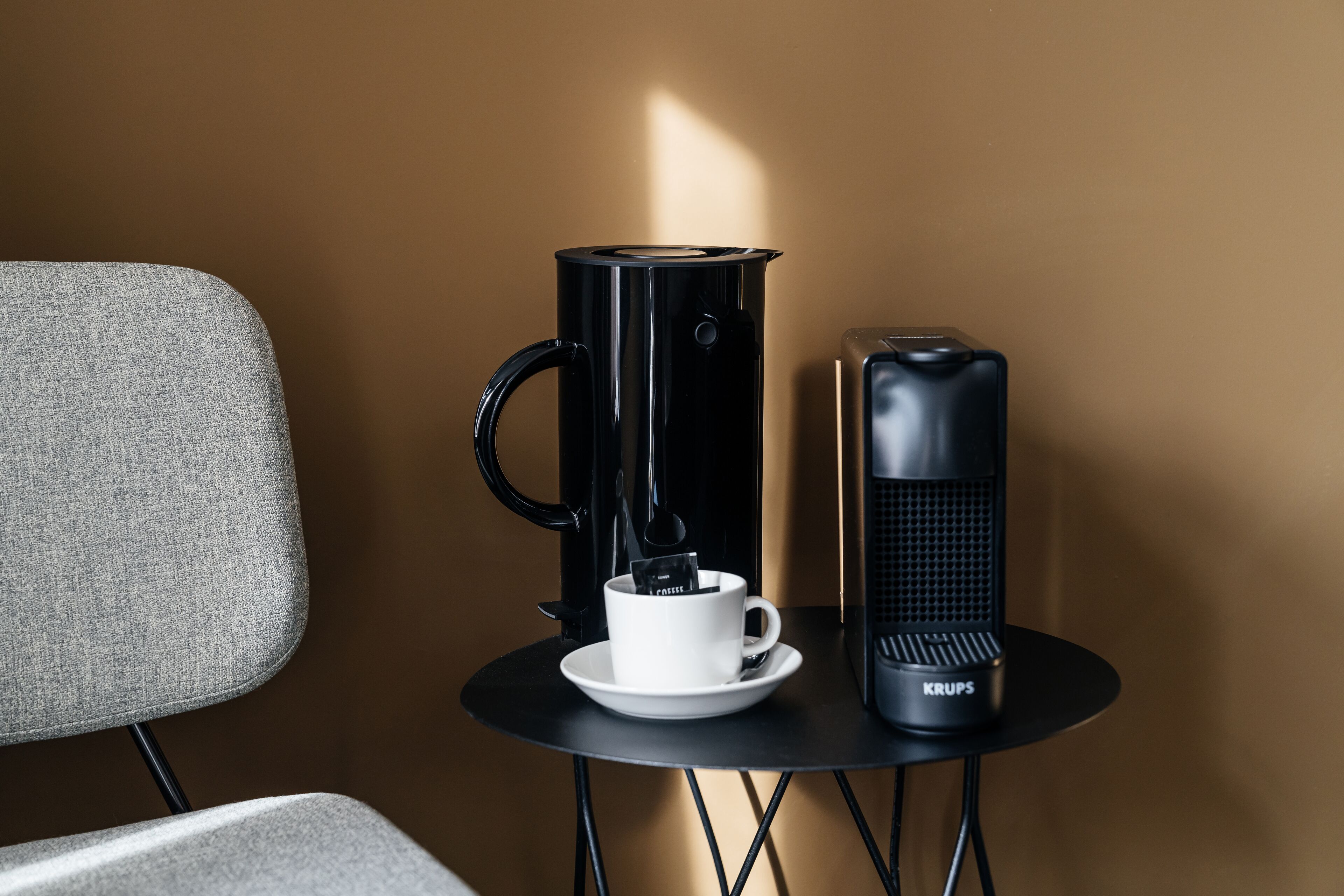 Une petite table avec une machine à café, une tasse et un radiateur électrique Krups.