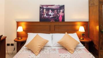 Habitación de hotel con cabecera de madera, dos lámparas de noche, cama con ropa de cama floral y un cuadro sobre la cabecera.