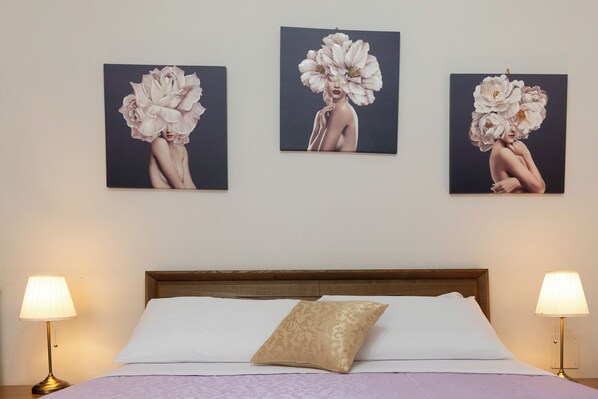 A hotel room with a bed, two bedside lamps, and three wall-mounted paintings of floral designs.