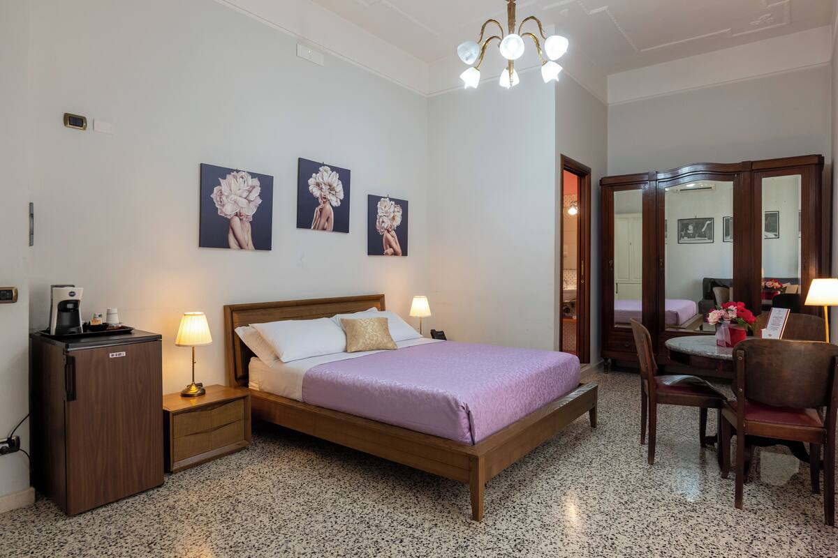 Ein Hotelzimmer mit Bett, Nachttischen, Schreibtisch mit Stuhl, Spiegel und einem Kunstwerk an der Wand.