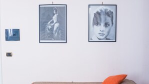Ein Zimmer mit einem Bett, einem Tisch mit Blumenvase und zwei gerahmten Bildern an der Wand.
