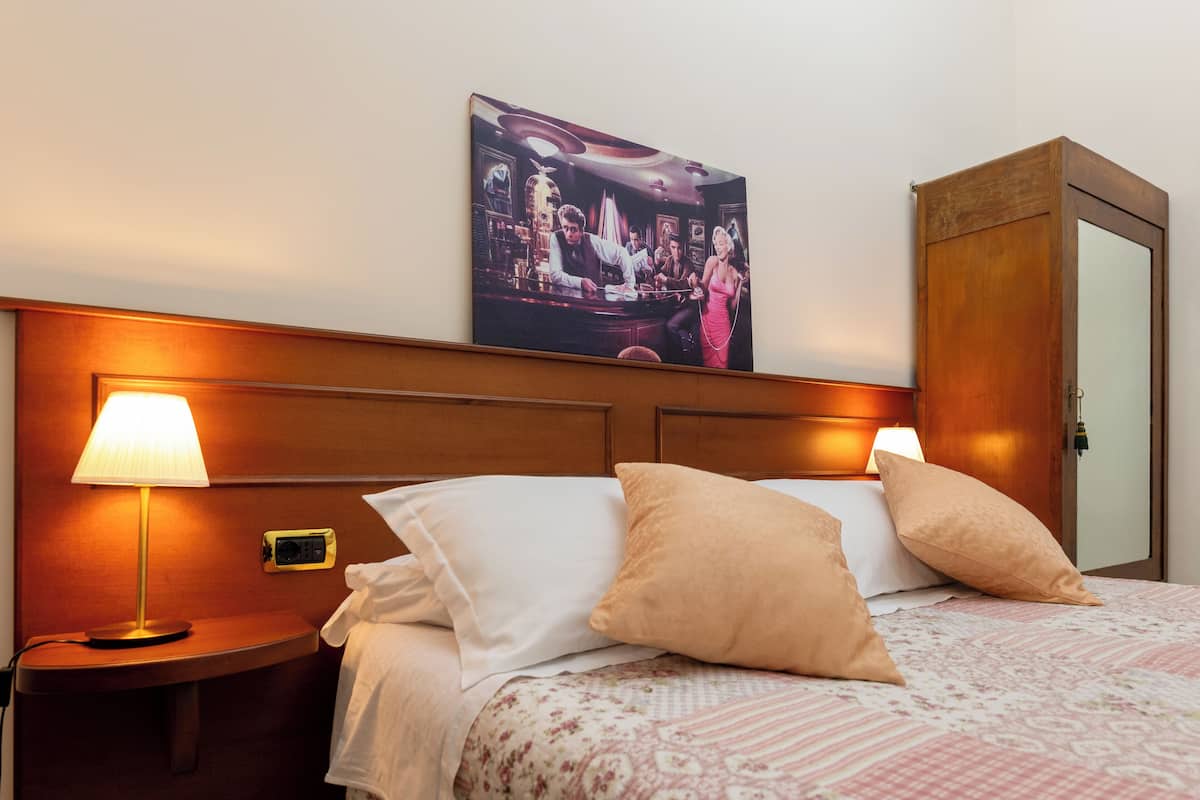 Ein Hotelzimmer mit einem Bett, zwei Nachttischlampen, einem Nachttisch, einem Holzschrank und einem gerahmten Bild an der Wand.