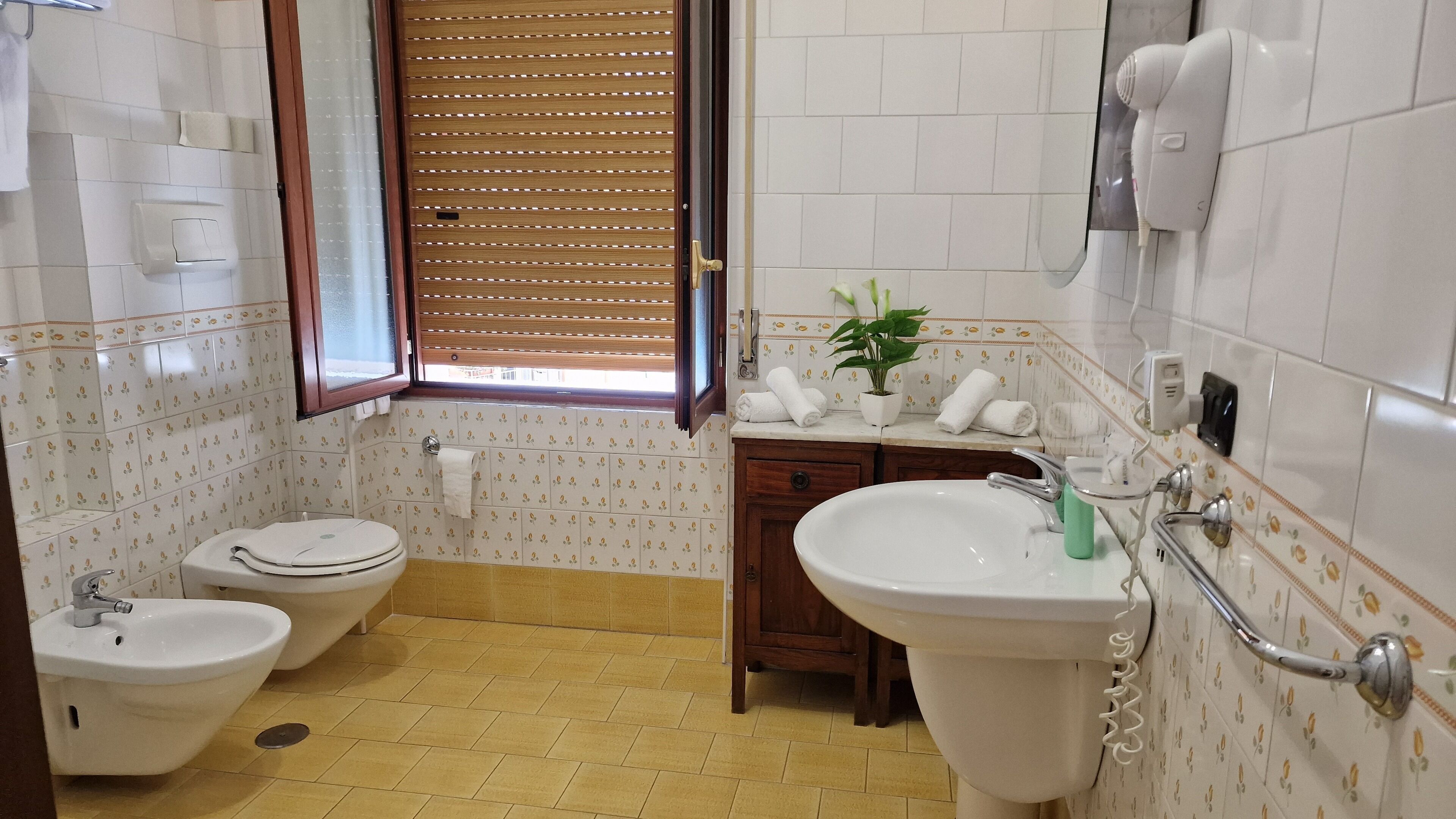 Ein Badezimmer mit Toilette, Bidet, Waschbecken und einem Fenster mit Jalousien.