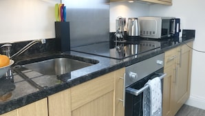 A modern kitchen with a black granite countertop, stainless steel sink, wooden cabinets, and a microwave. - Lux Blu - Truro Apartment (Truro)
