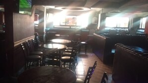 Un interior de restaurante con varias mesas redondas y cabinas, piso de madera y una zona de bar.