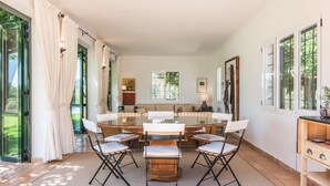 Uma sala de jantar ampla com mesa redonda e cadeiras, um sofá e vista para o verde lá fora.