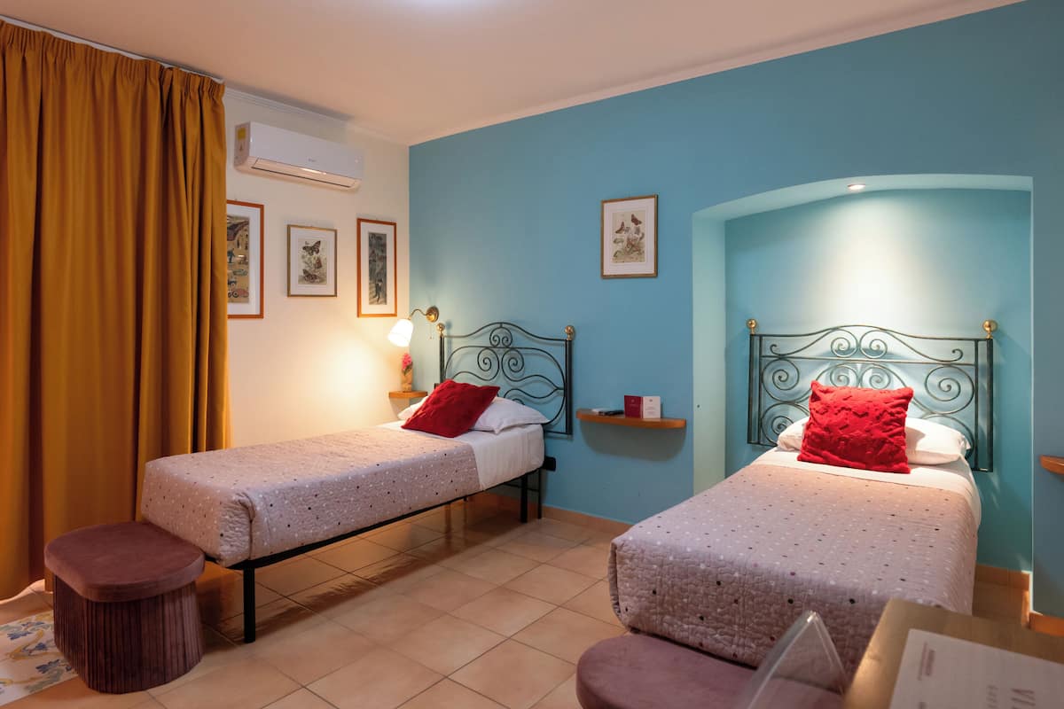 A room with two single beds, a wooden stool, a small table, and a wall-mounted shelf.