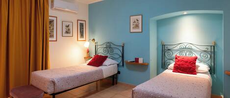 A room with two single beds, a wooden stool, a small table, and a wall-mounted shelf.