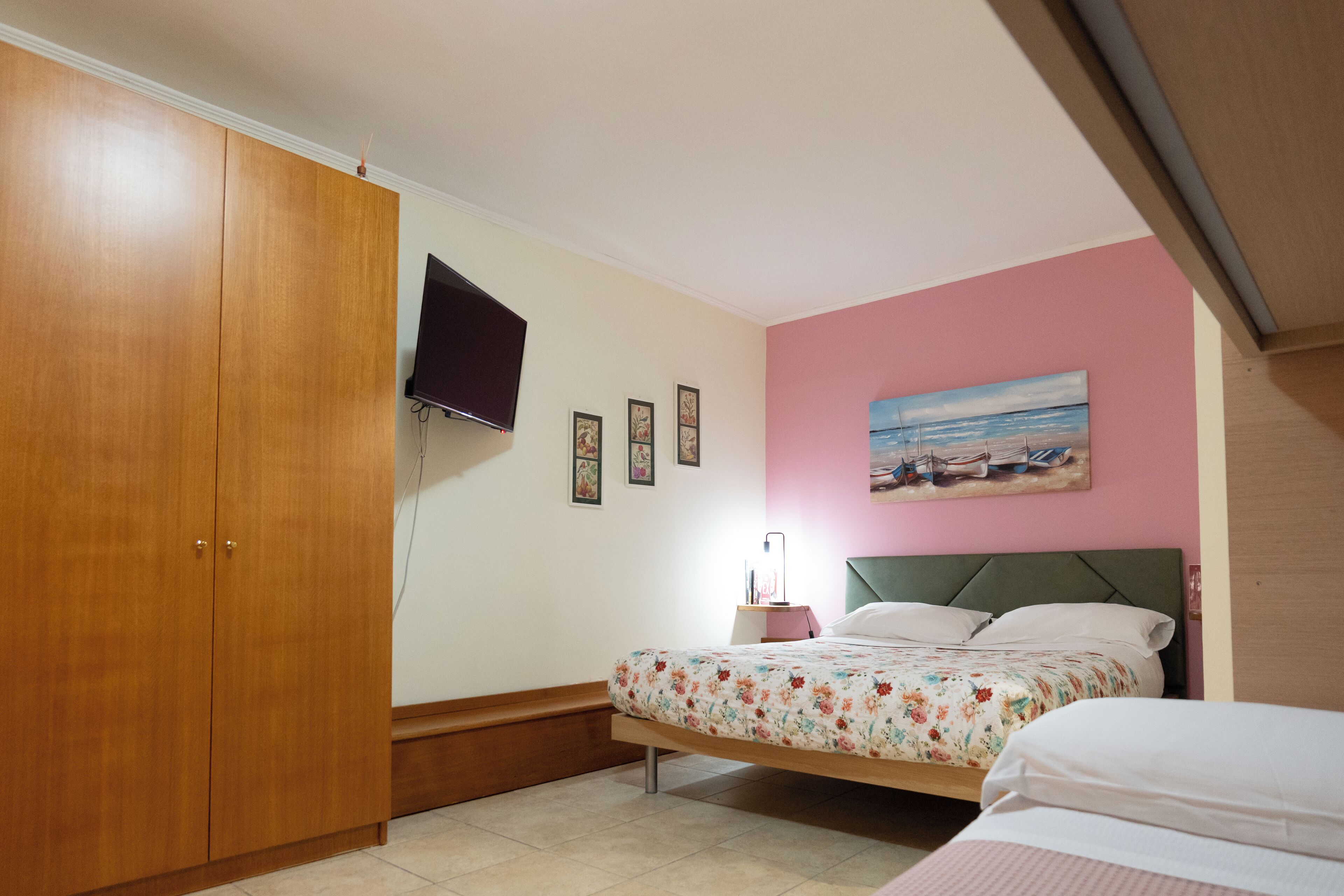 A bedroom with a bed, a wardrobe, a TV mounted on the wall, and a painting above the bed.