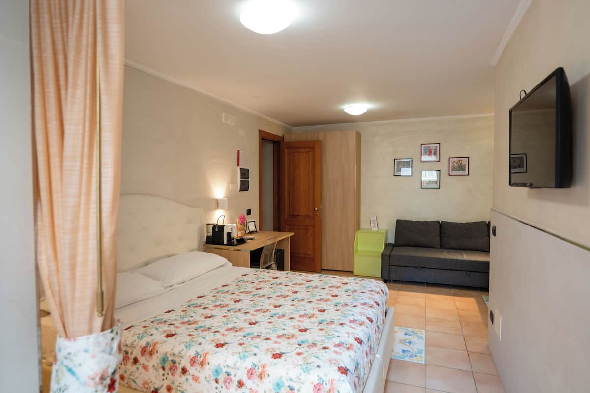 A bedroom with a bed, a desk, a sofa, and a TV.