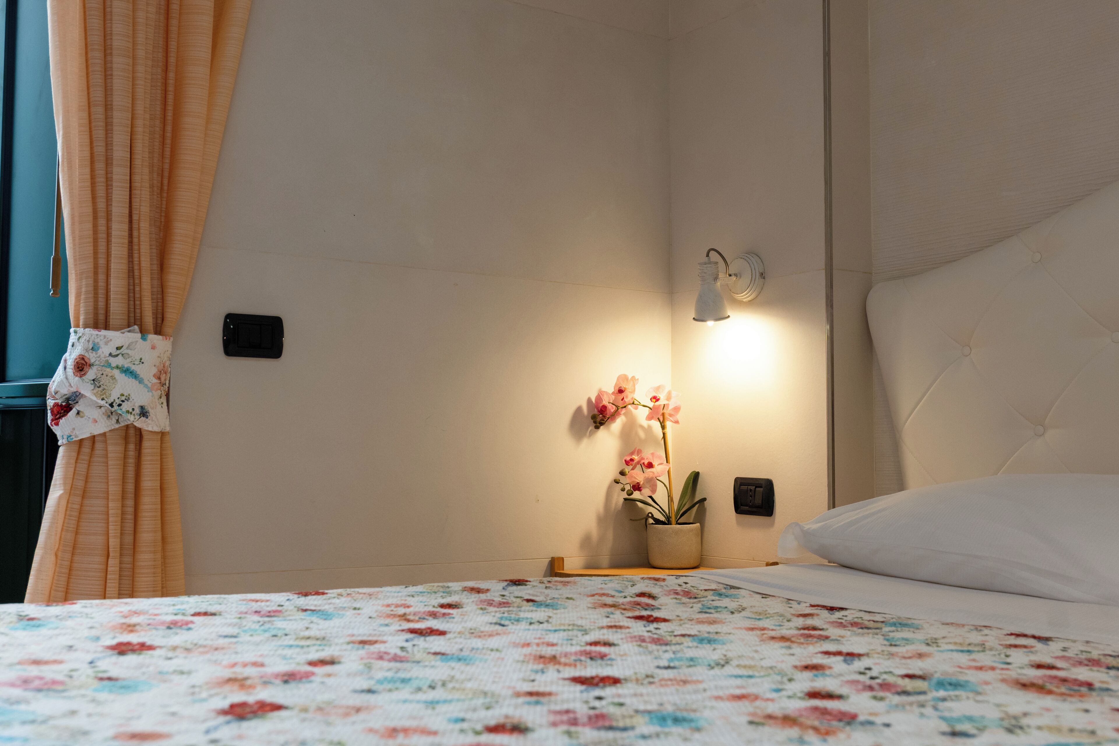 Un dormitorio con cama, una mesita de noche, una orquídea en maceta y una lámpara de pared.