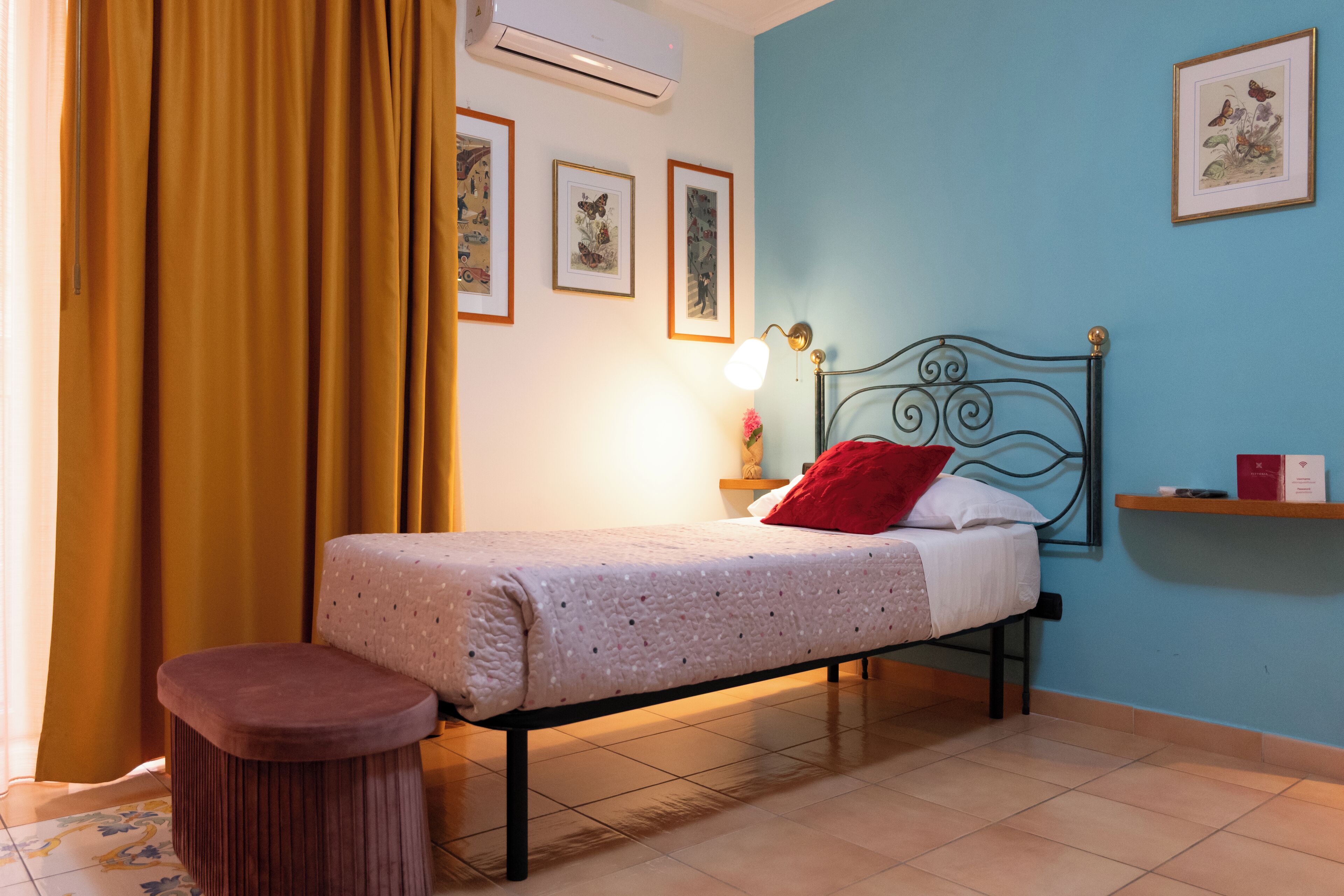 A neatly arranged bedroom with a bed, a bedside table, a small stool, and a wall-mounted shelf.