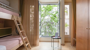 Una habitación con literas, una escalera, una mesita y un ventanal con cortinas.
