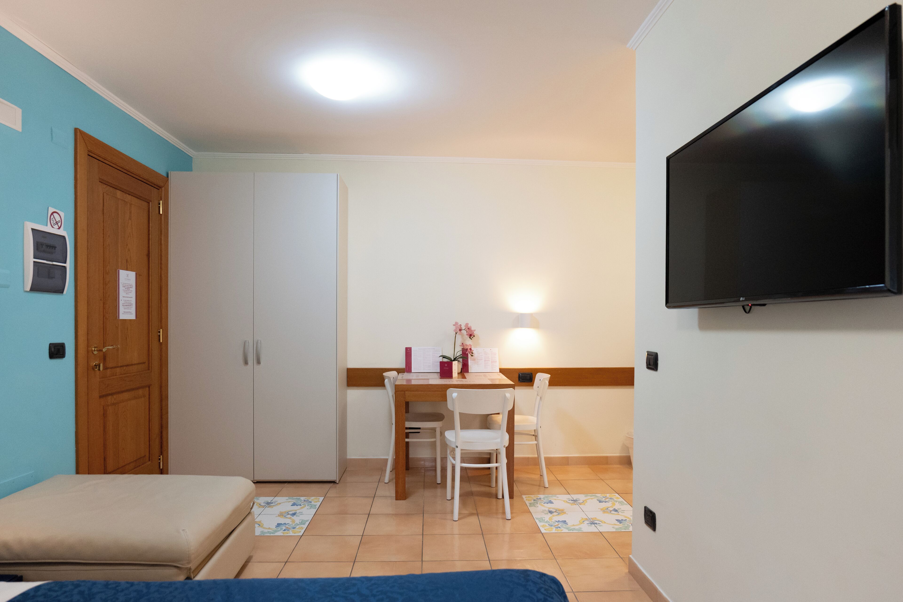 A room with a bed, a desk with chairs, a television, and a door.