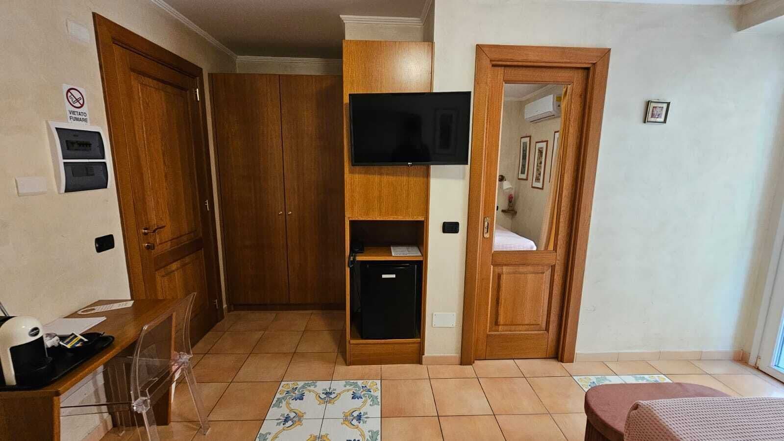 Ein Zimmer mit einem Holzschrank, einem fest eingebauten Fernseher, einer kleinen schwarzen Vitrine und einem Fliesenboden.