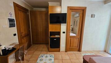 A room with a wooden wardrobe, a built-in TV, a small black cabinet, and a tiled floor.
