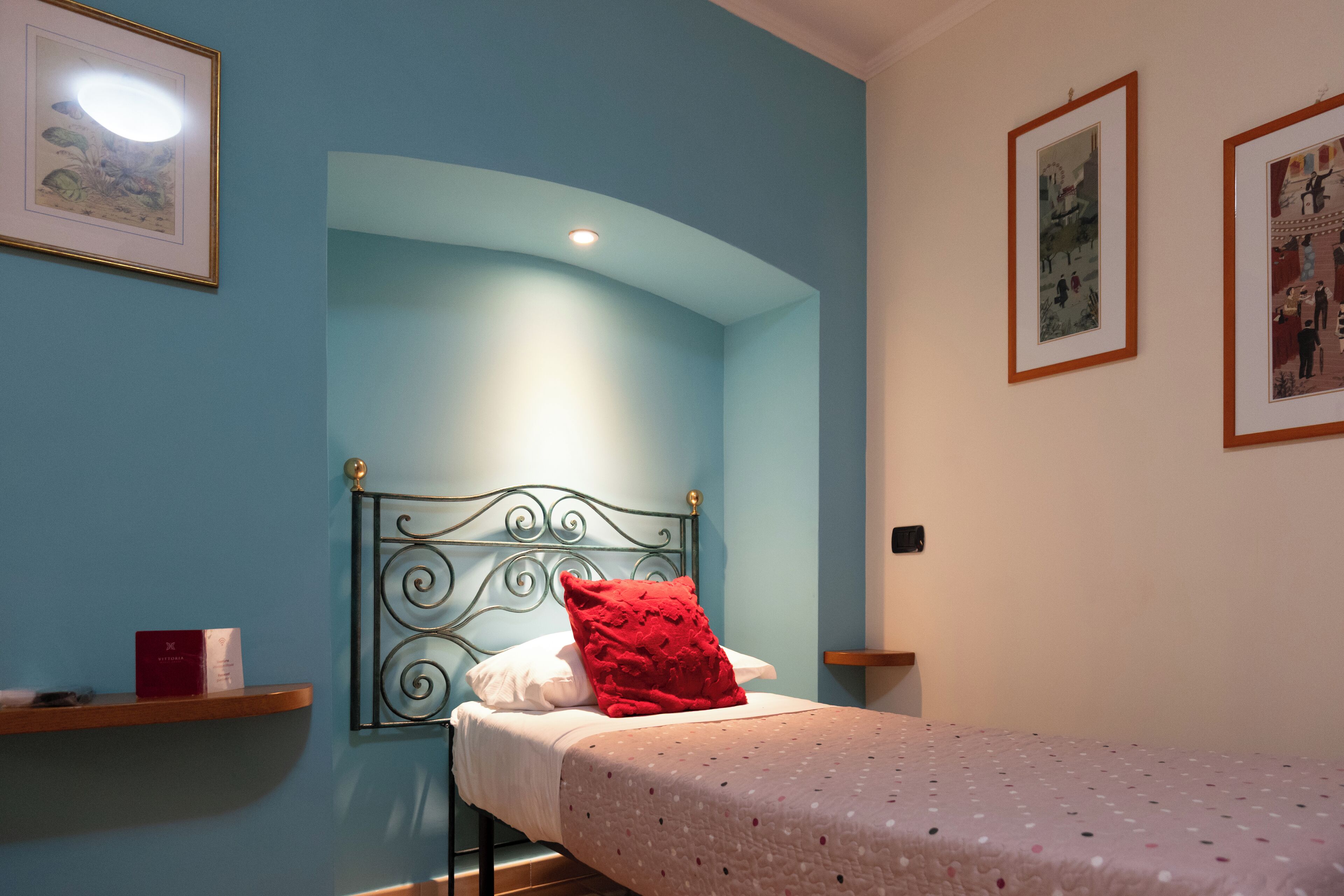 A single bed with a red pillow, a headboard, and a light blue wall.