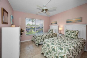 A bedroom with two beds, a ceiling fan, a window with blinds, and a refrigerator.