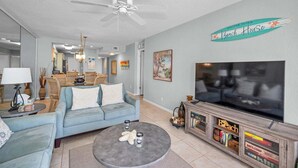 A living room with a sofa, coffee table, TV, and a ceiling fan. - Waterfront 2BR/2BA condo in St. Petersburg with pool, hot tub, and beach access. (St. Petersburg)
