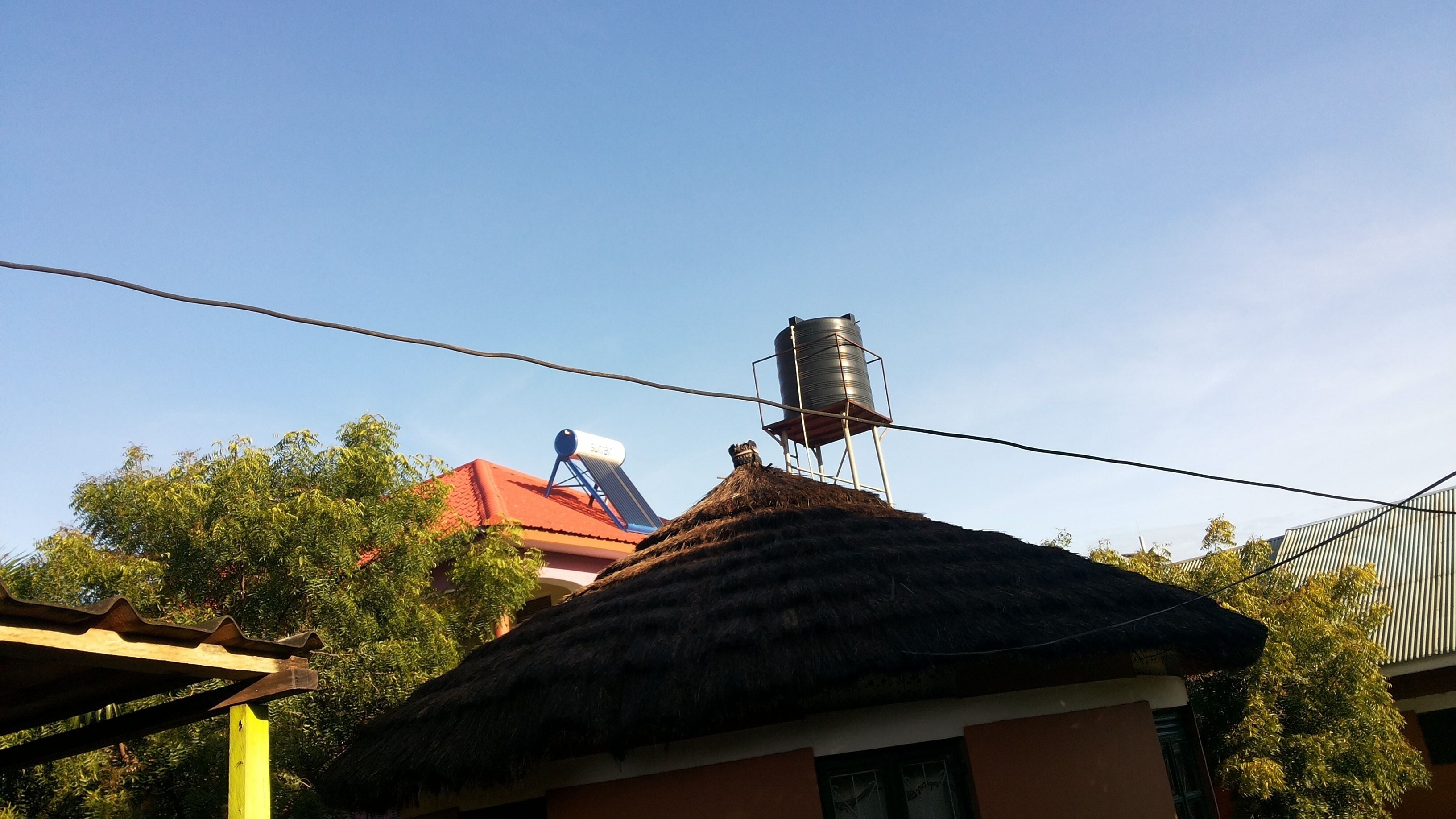 A thatched-roof house with a water tank on a metal stand.