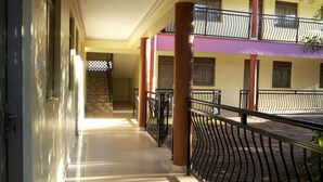 Un couloir au sol carrelé, un escalier et un balcon doté d’une rambarde en métal.